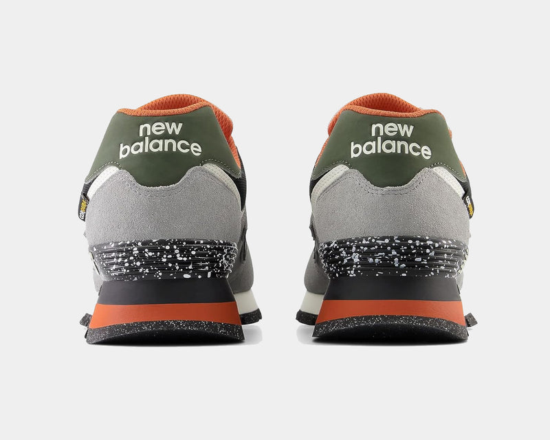 New Balance 574 Rugged sneakers back view featuring gray suede upper, green heel tab, orange details, and speckled black midsole.