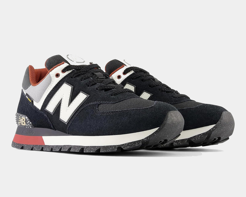 New Balance 574 Rugged sneakers in black suede with white "N" logo, gray and rust accents, and rugged speckled outsole, angled view.