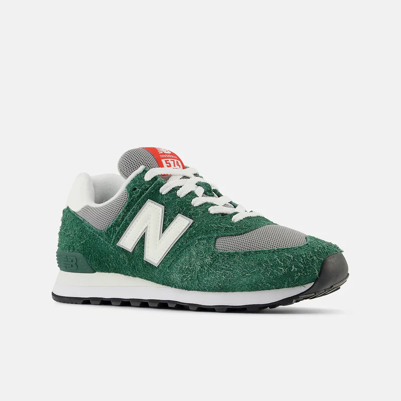 New Balance 574 sneakers with green textured suede upper, gray mesh details, white leather logo overlay, and red branding, angled front view.