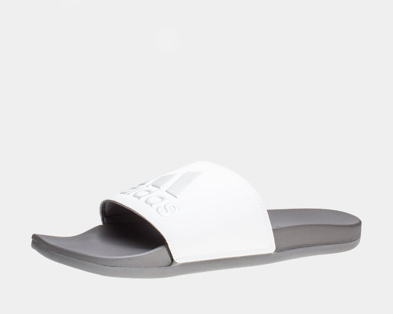 Adidas Adilette Comfort Slides in white with logo details on soft strap and gray cushioned sole, angled side view.