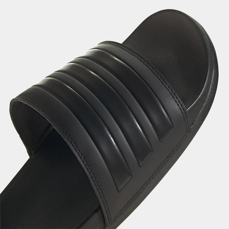Adidas Adilette Comfort Slides in black with textured strap and cushioned footbed, angled close-up view.