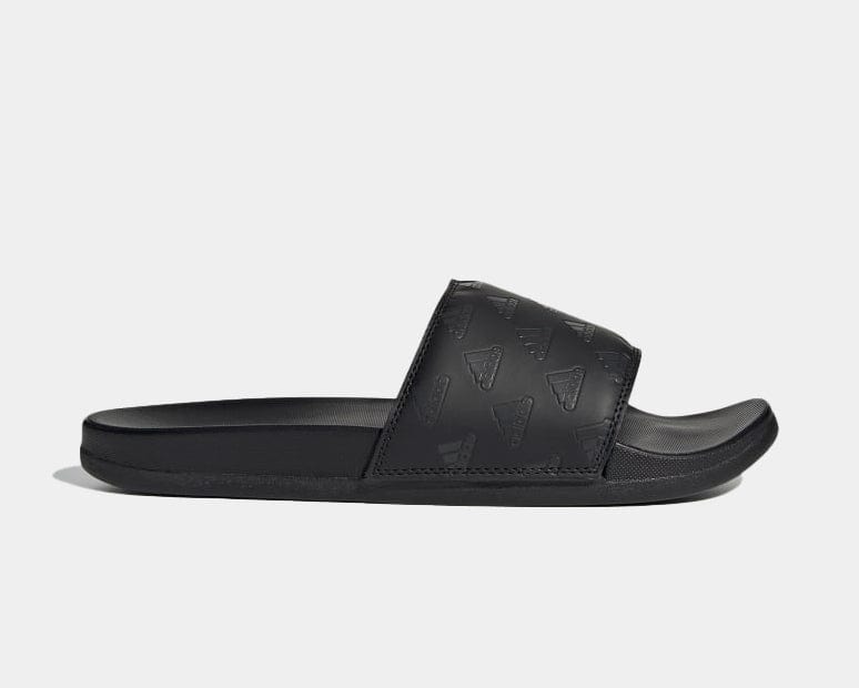 Adidas Adilette Comfort slides in black with embossed Adidas logo patterns and cushioned footbed, side view.