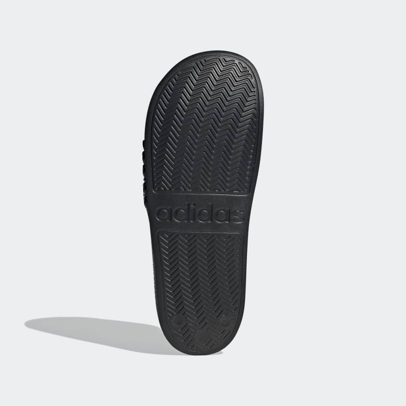 Adidas Adilette Shower Slides outsole in black showing textured herringbone traction pattern and embossed logo, sole/bottom view.