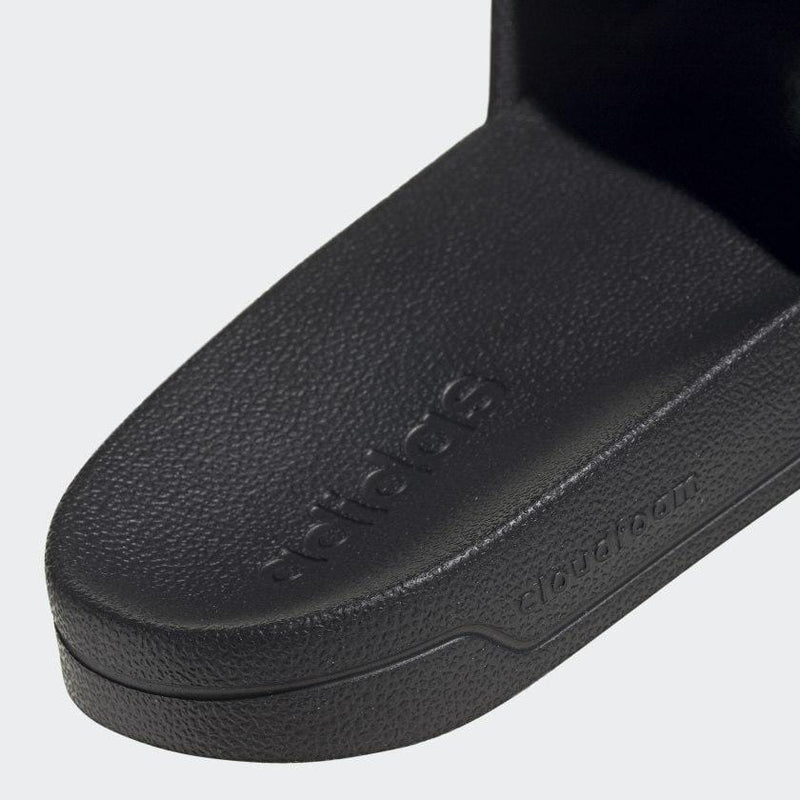 Adidas Adilette Shower Slides in black with textured Cloudfoam footbed, close-up view of branding and sole detailing.