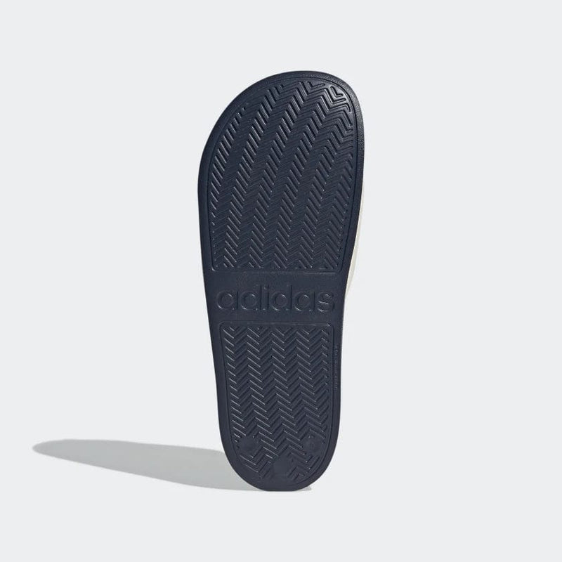 Adidas Adilette Shower Slides sole view showing navy blue rubber outsole with herringbone traction pattern and embossed branding.