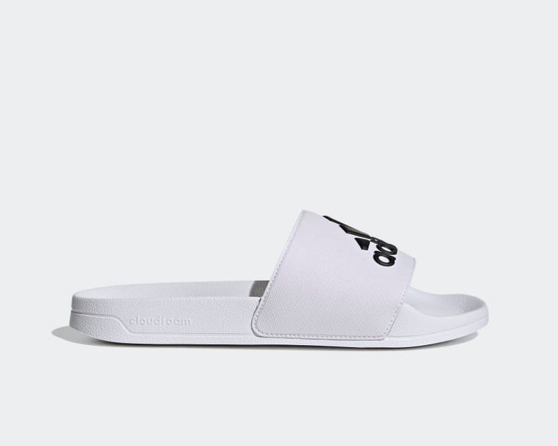 Adidas Adilette Shower Slides in white with black logo, Cloudfoam footbed and textured strap, side view.