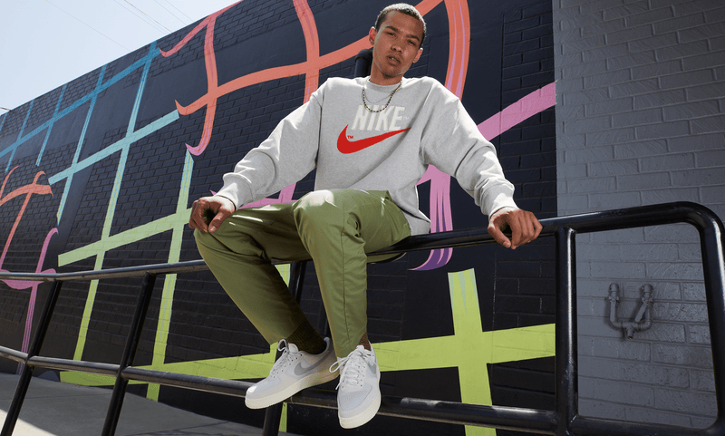 Nike Air Force 1 '07 LV8 sneakers in white with gray accents, worn by sitting individual in urban setting, front lifestyle view.