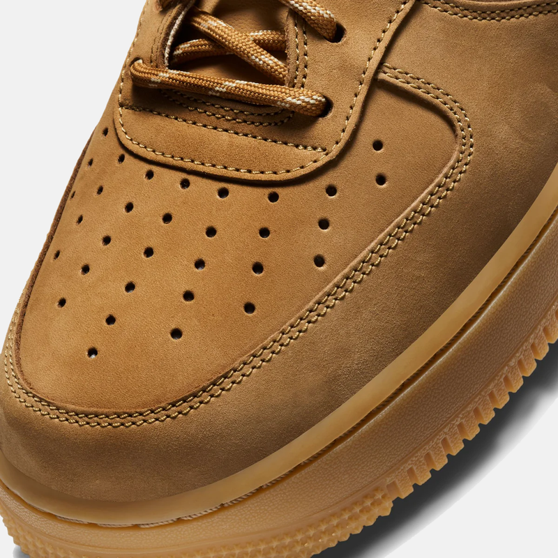 Close-up of a brown suede shoe with perforated design on a white background