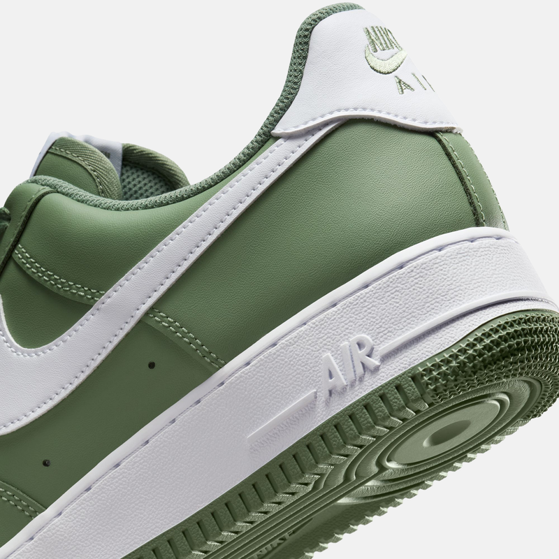 Nike Air Force 1 '07 sneakers in olive green and white with leather upper and embossed "AIR" text on the midsole, angled heel view.