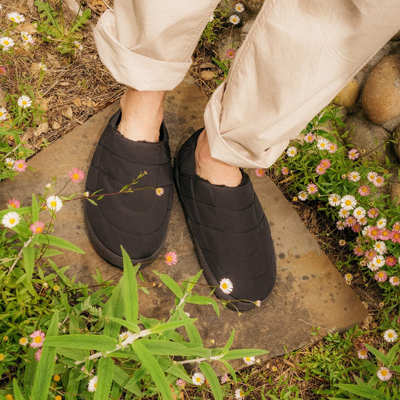 SeaVees Apres Puff Slip On shoes in black with quilted design and cushioned soles, worn outdoors on a garden pathway.