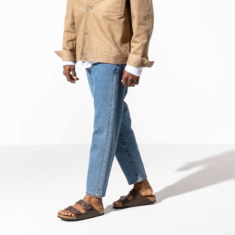Birkenstock Arizona Birko-Flor® sandals in dark brown with adjustable buckled straps and contoured cork footbed, worn by person walking.