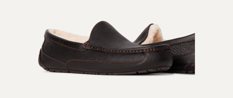 UGG Ascot Leather slippers in dark brown leather with contrast stitching and soft shearling lining, side angled view.