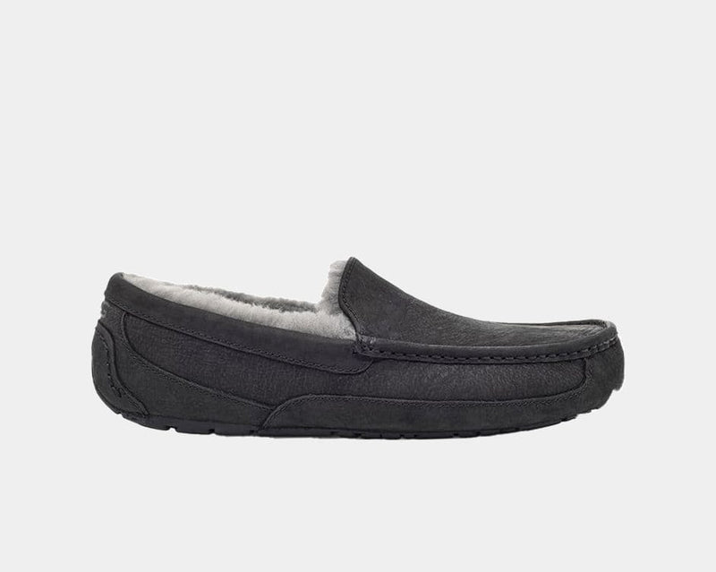 UGG Ascot Matte Leather slippers in black with plush lining and moccasin stitching, side view.