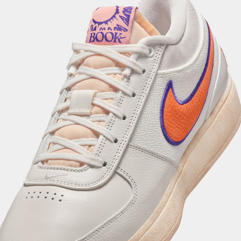 Nike Book 1 Decade sneakers in white leather with orange Swoosh, purple accents, and peach tongue, close-up side view.