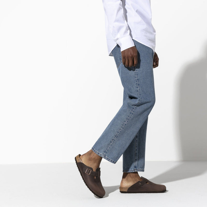 Birkenstock Boston Oiled Leather clogs in dark brown with adjustable strap and cork footbed, worn by a person walking.