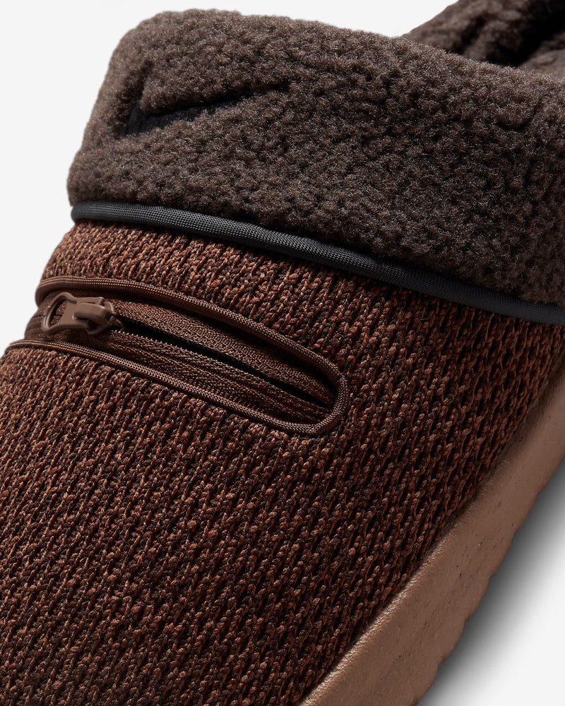 Nike Burrow SE slippers in brown with textured knit upper, zippered pocket detail, and plush fleece collar, close-up side view.