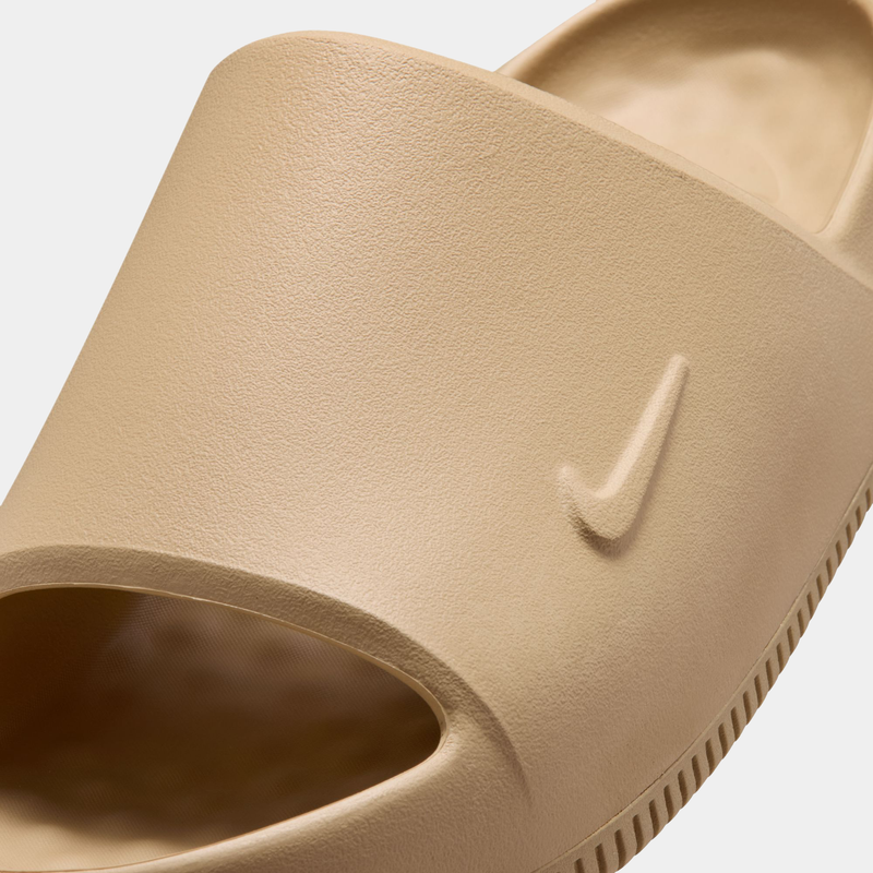 Nike Calm Slide 2.0 slides in beige with textured finish, debossed Swoosh logo, and open toe design, close-up view.
