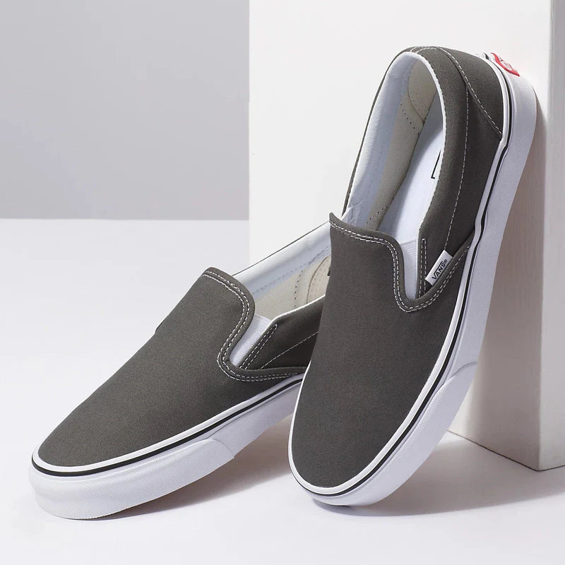 Vans Classic Slip On shoes in dark gray canvas with white rubber sole and elastic side accents, angled pair view.