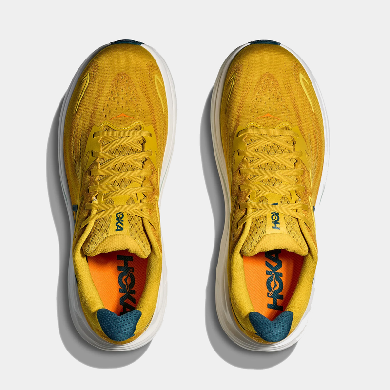 HOKA Clifton 10 running shoes in golden yellow with breathable mesh upper, cushioned orange insoles, and teal accents, top view.