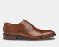 Johnston & Murphy Conard Cap Toe dress shoes in tan leather with brogue detailing and stacked heel, side view.