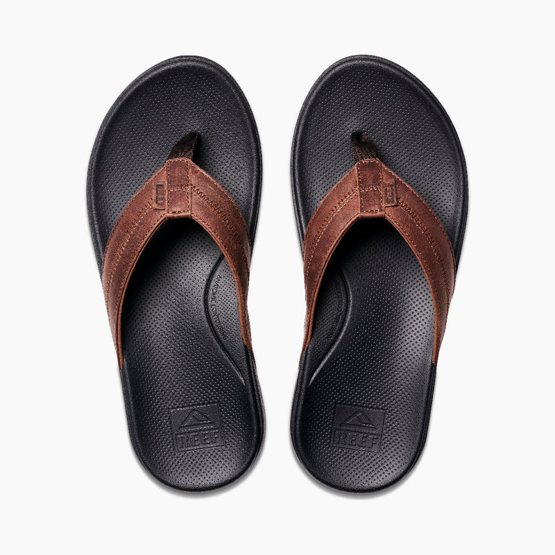 Reef Cushion Phantom 2.0 LE flip-flops with brown leather straps and black cushioned footbeds, top view.
