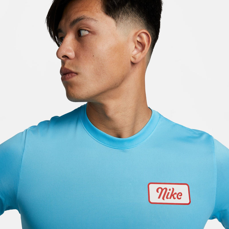 Nike Dri-FIT Fitness T-Shirt in light blue with red Nike logo patch, showcasing moisture-wicking fabric, front view.