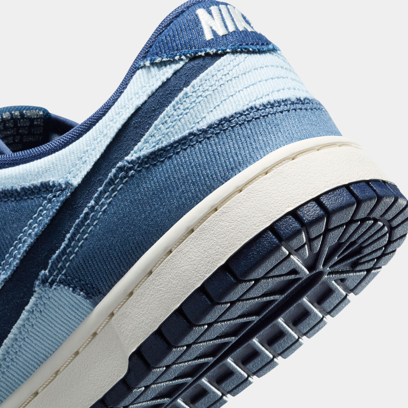 Nike Dunk Low Retro SE sneakers, close-up of heel area in blue denim and light blue accents with textured outsole in navy and white.