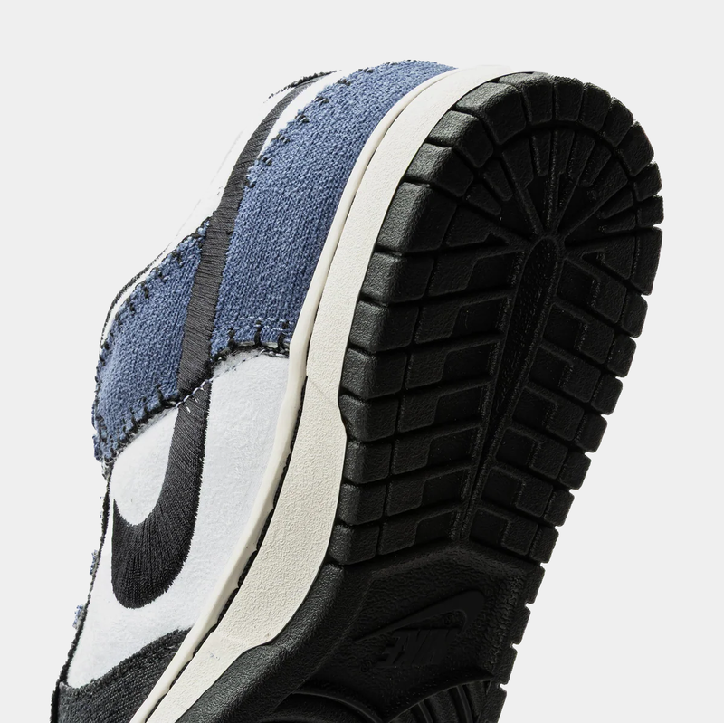 Nike Dunk Low Retro sneakers close-up of outsole and textured upper featuring denim blue overlays, black accents, and rubber black sole.