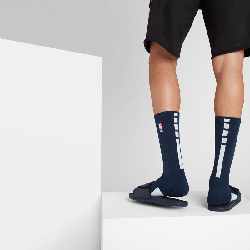 Nike Elite Crew socks in navy blue with white vertical stripe design and NBA logo, back view worn with sandals.