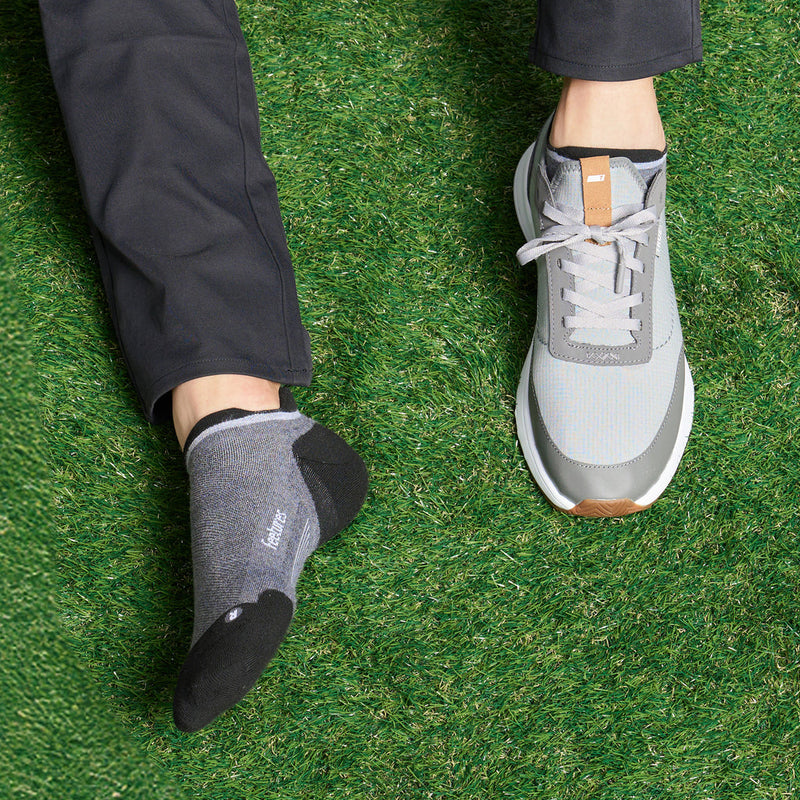 Feetures Elite Golf Max Cushion No Show Tab socks in gray and black, worn on grass.