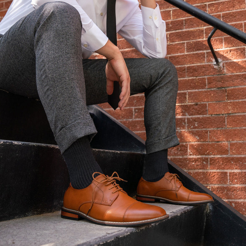 Feetures Everyday Max Cushion Crew socks in black, soft fabric with extra cushioning, worn by seated man in formal shoes.