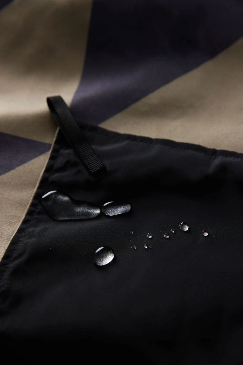 Nomadix Festival Blanket in multicolor geometric design with black water-resistant corner featuring water droplets.