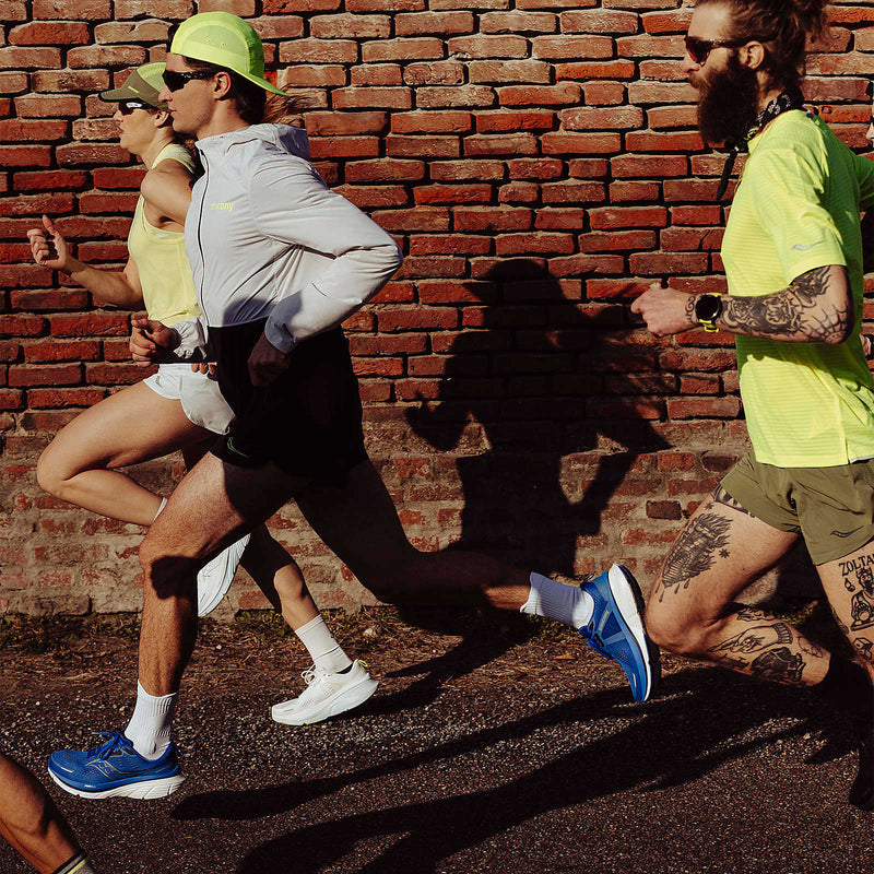 Saucony Guide 18 running shoes in blue with white midsoles and mesh uppers, worn by runner in motion alongside others.