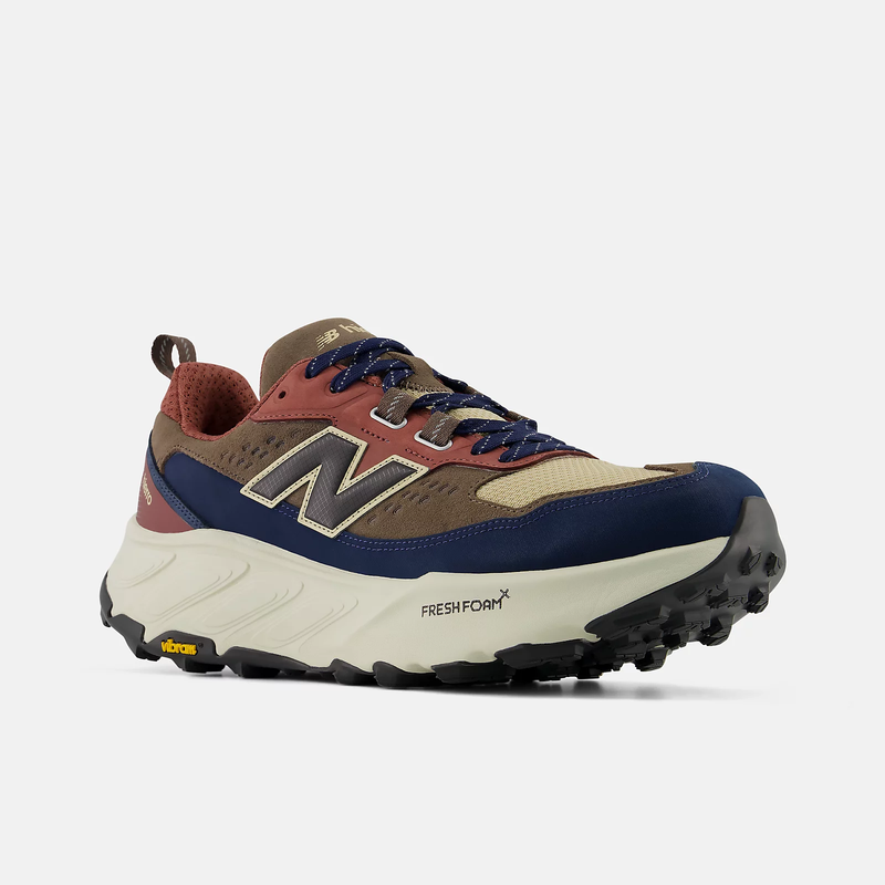 New Balance Hierro Trek hiking shoes with a tan and navy upper, rust red accents, Fresh Foam midsole, and Vibram outsole, angled front view.