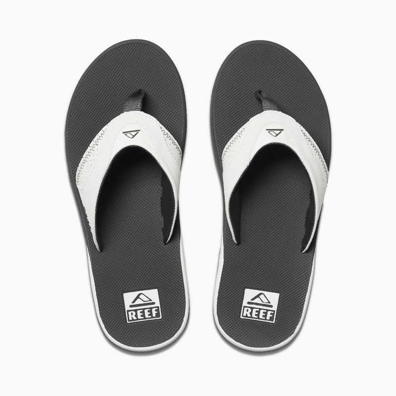 Reef Leather Fanning flip flops with black textured footbed, white leather straps, and logo detailing, top view.