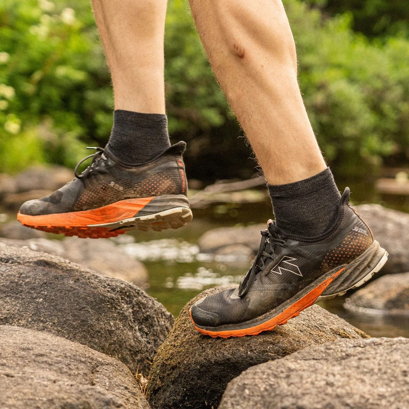 Darn Tough Light Hiker Quarter Lightweight Hiking Socks in charcoal gray, moisture-wicking and cushioned, worn outdoors on rocky terrain.