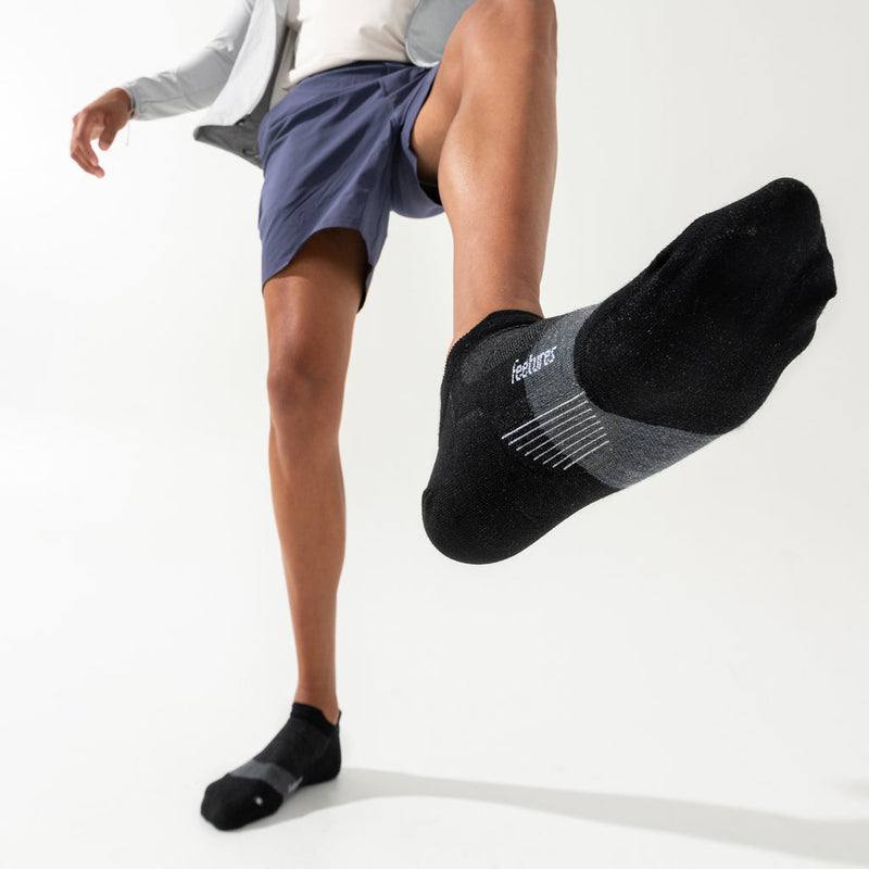 Feetures Merino 10 Ultra Light Cushion No Show Tab socks in black with gray accents and moisture-wicking fabric, lifestyle view worn by person in motion.