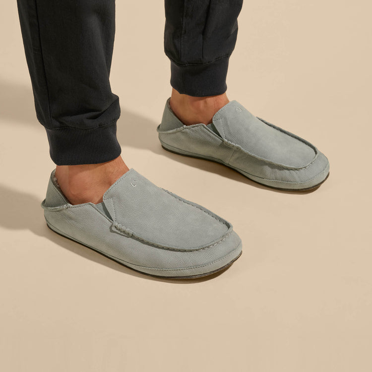 OluKai Moloa Slipper casual shoes in light gray suede with moc toe design, worn by person indoors.