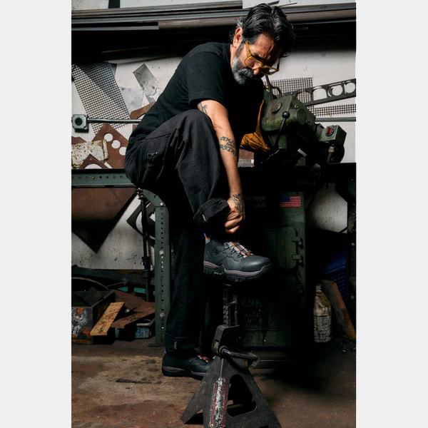 DC WorkCrew Navigator Work Hi Top Comp Toe work boots in black with red and gray accents, worn by a worker in an industrial setting.