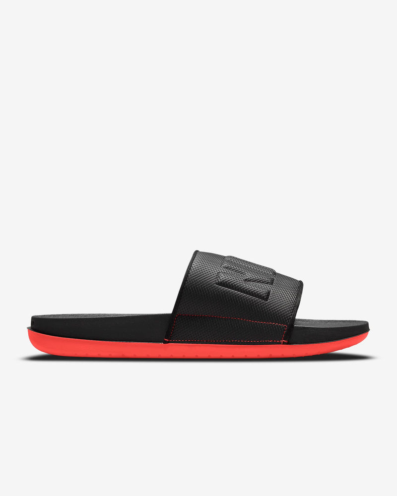Nike Offcourt Slide sandals in black with textured strap and bright red cushioned sole, side view showing sleek design.