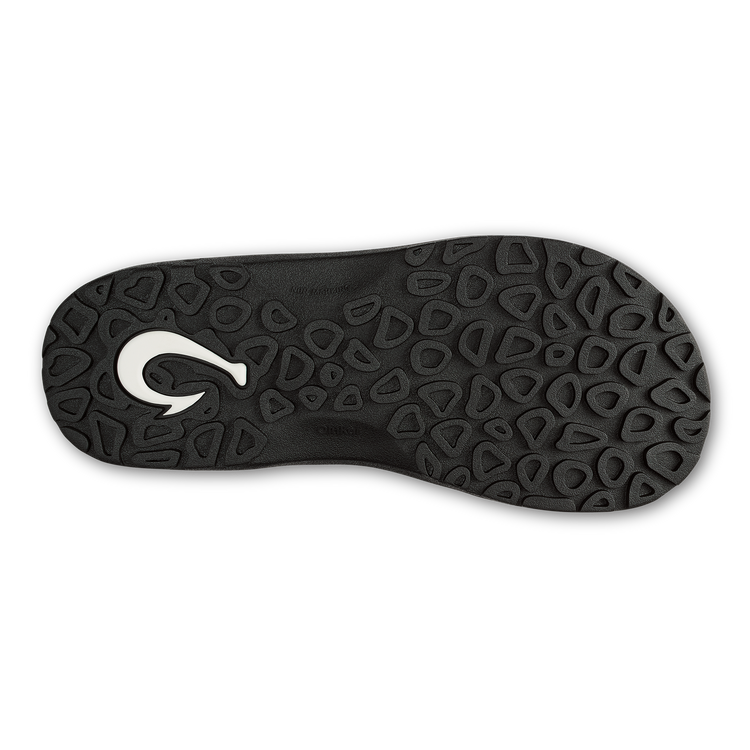 OluKai ʻOhana Pālua sandals outsole in black rubber with textured pattern and white hook logo, sole/bottom view