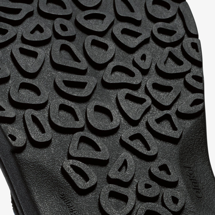OluKai ʻOhana Pālua sandal outsole in black, featuring textured tread pattern for enhanced traction, sole/bottom view.