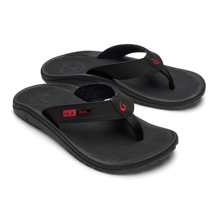 OluKai ‘Ohana sandals in black with red logo accents, water-resistant strap and cushioned footbed, angled side view.