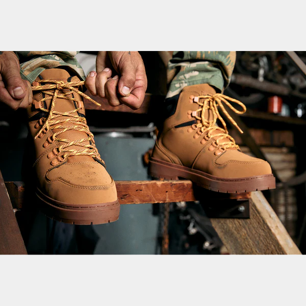 "DC WorkCrew Peary TR Work Waterproof Comp Toe Boot in tan leather with yellow laces and rugged outsole, lifestyle view of person tying shoelace"