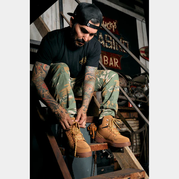 DC WorkCrew Peary TR Work Waterproof Comp Toe Boot in tan leather with lace-up design and durable sole, worn by man tying laces in workshop setting.