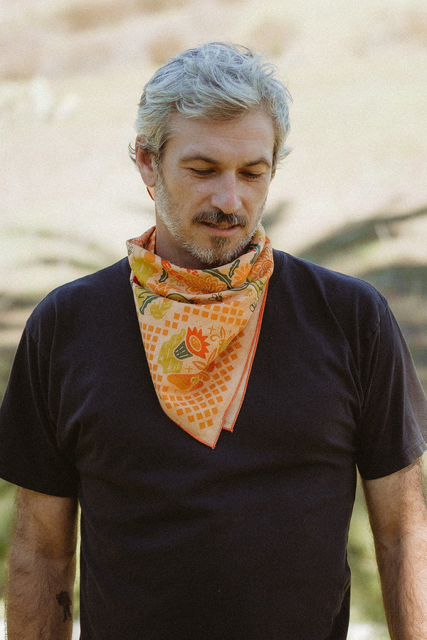 Bandits "Prickly Pollinators" bandana in vibrant orange with floral and cactus pattern, styled around the neck.