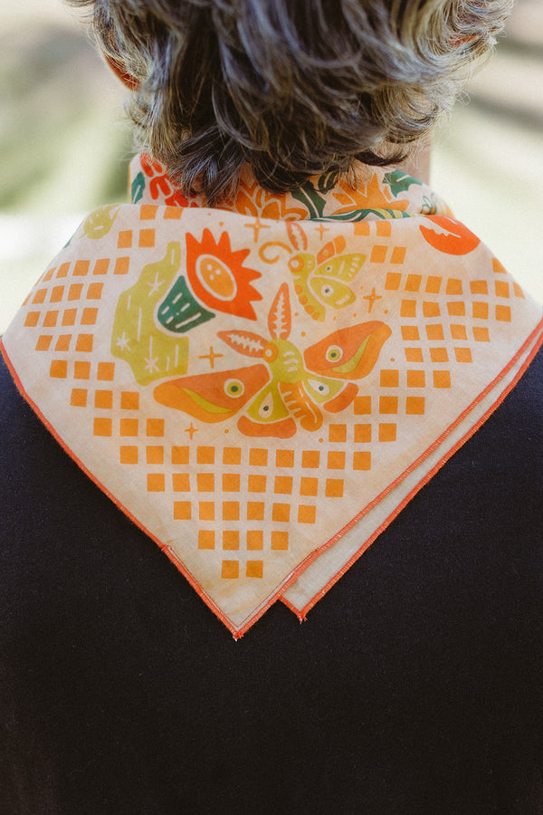 Bandits "Prickly Pollinators" bandana with orange, yellow, and green floral and insect illustrations, back view on wearer