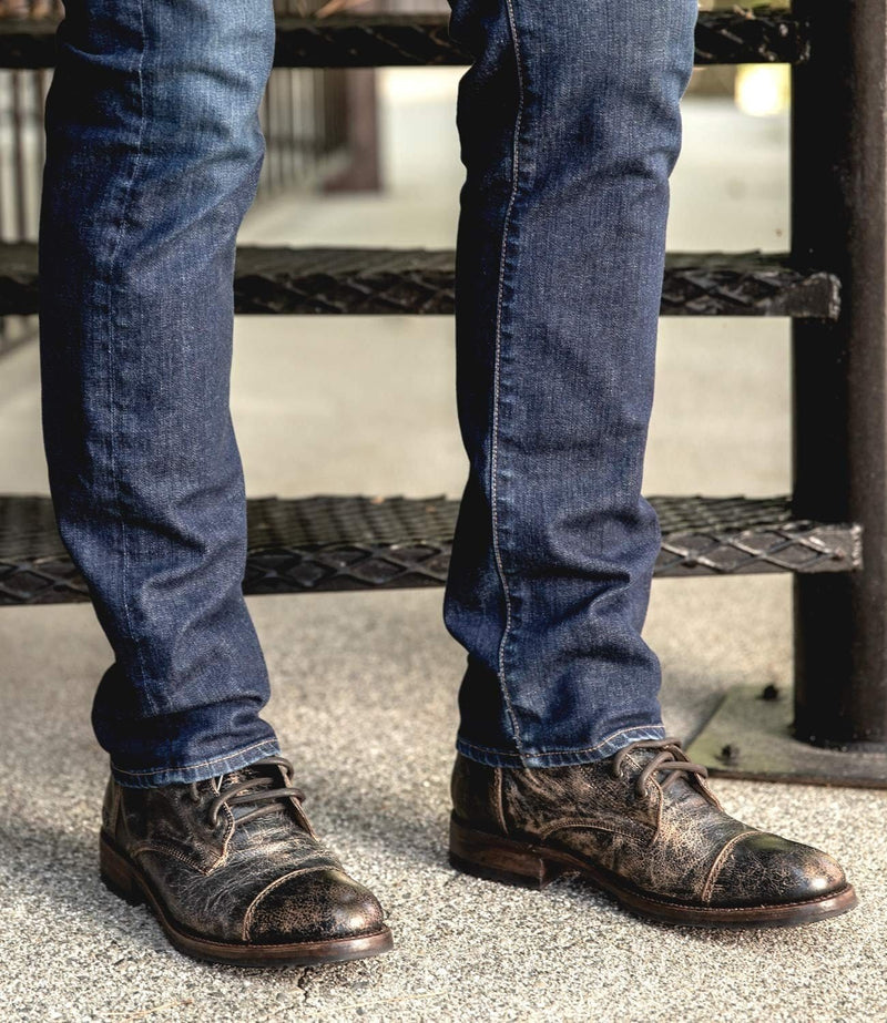 Bed Stu Protege boots in rustic brown leather with distressed finish and cap toe design, worn by person standing outdoors.
