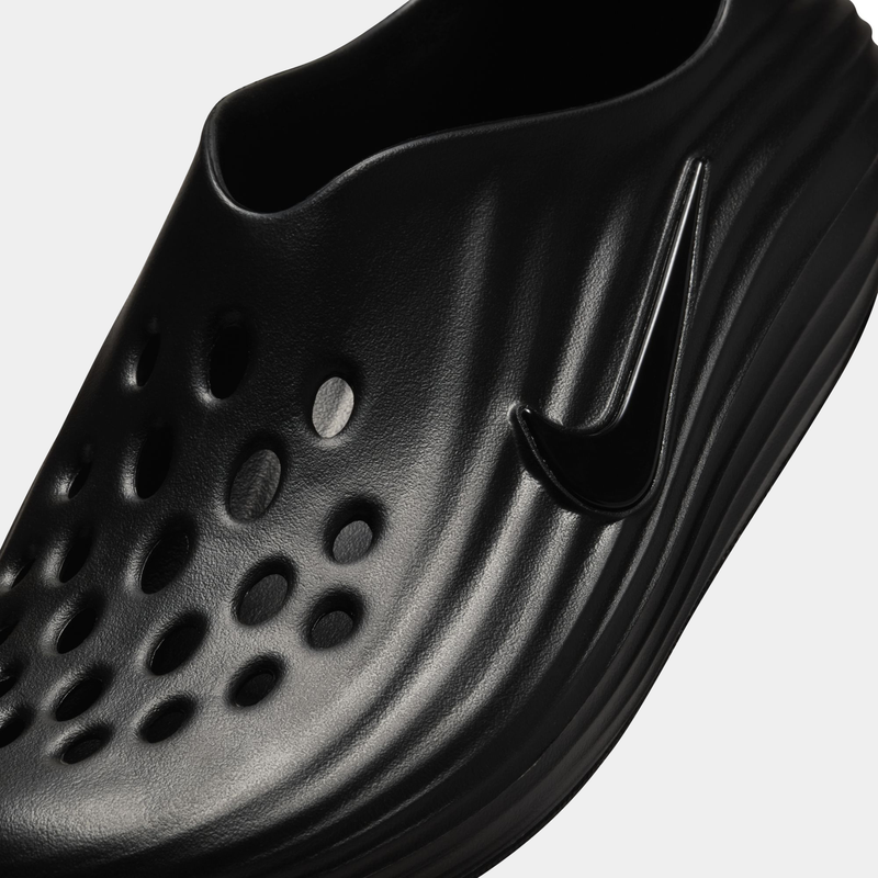 Nike ReactX Rejuven8 slip-on shoes in black, textured design with perforated details and embossed Nike Swoosh logo, close-up toe box view.