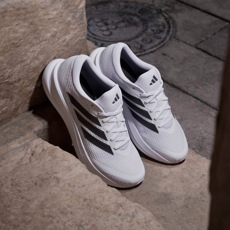 Adidas Runfalcon 6 running shoes in white with black stripes and mesh upper, angled side view resting on stone steps.